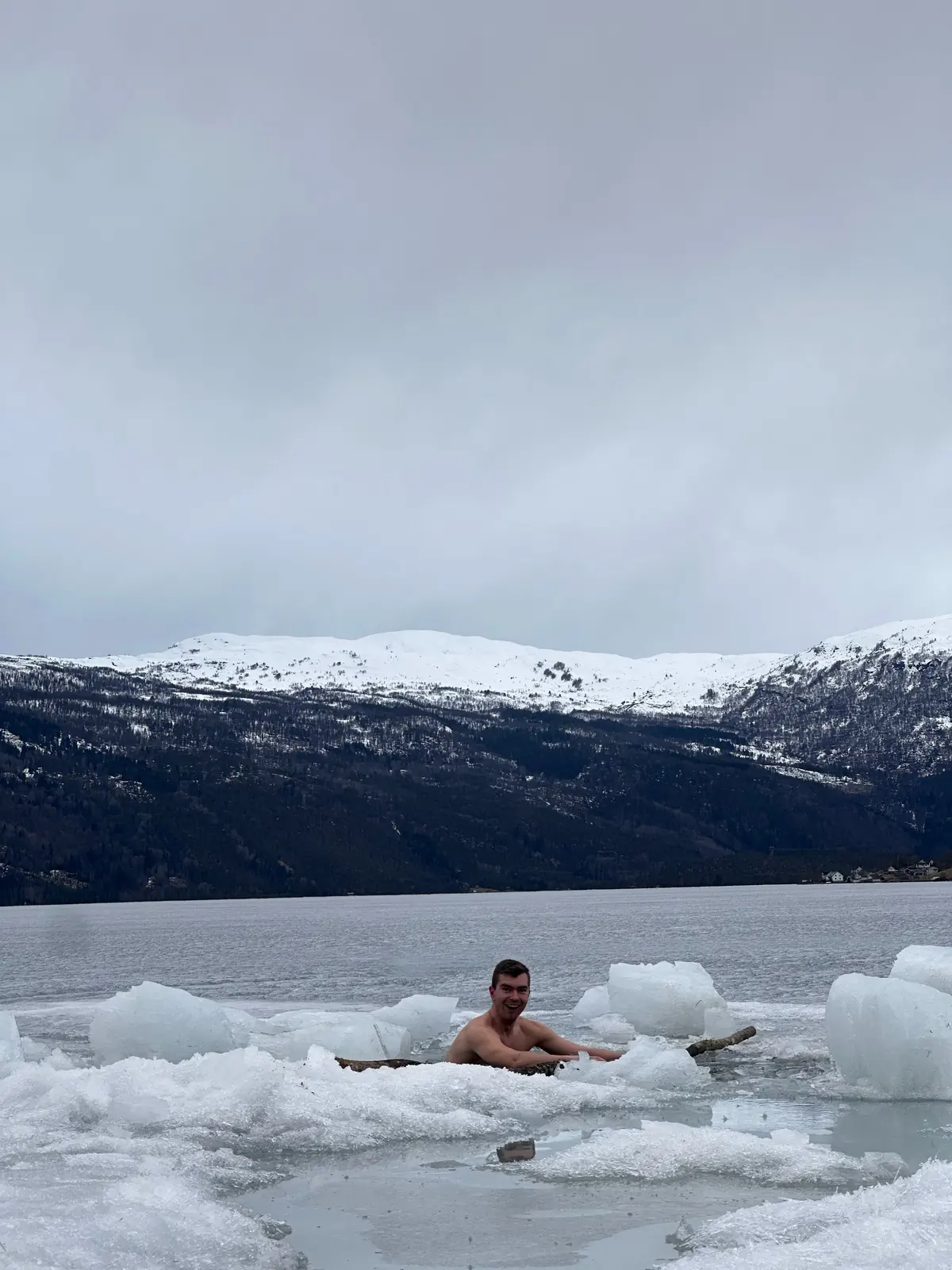 Deltaker bader i en råk i isen med snødekte fjell bak
